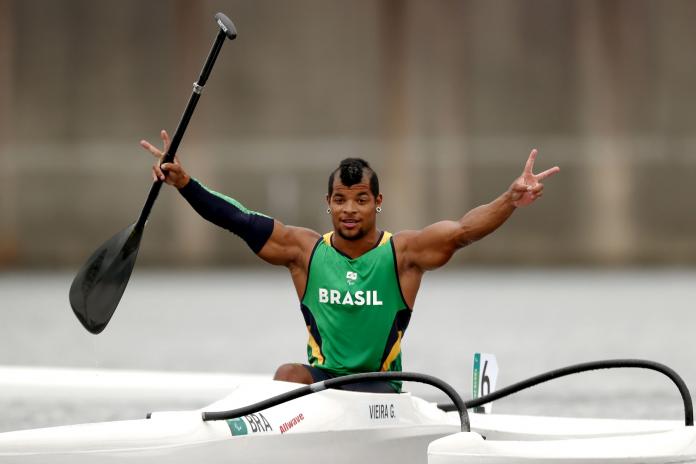 Giovane Vieira, a male Para canoe athlete from Brazil, raises his hands while sitting on a canoe boat.