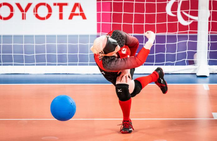 A female athlete throws a blue ball during a goalball game. 