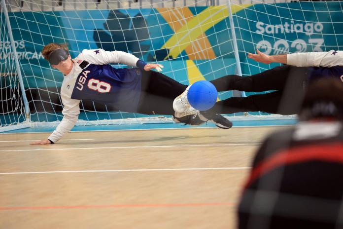A male athlete blocking a ball in front of the goal.