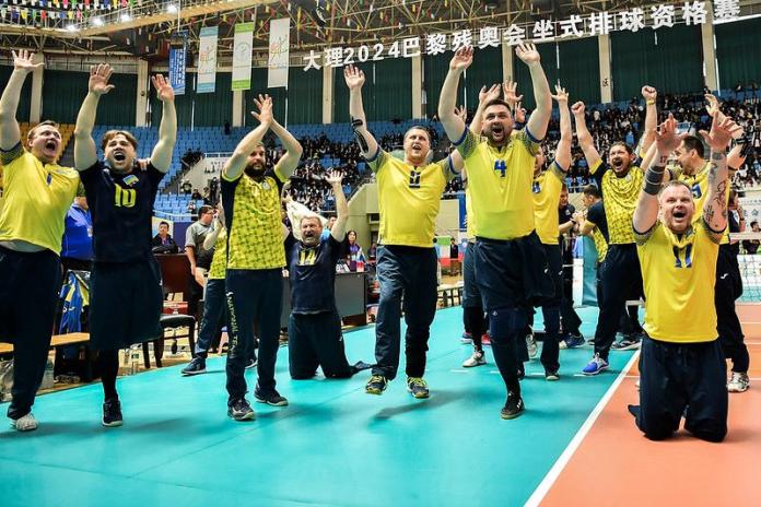 About 10 sitting volleyball athletes celebrate after qualifying for Paris 2024.