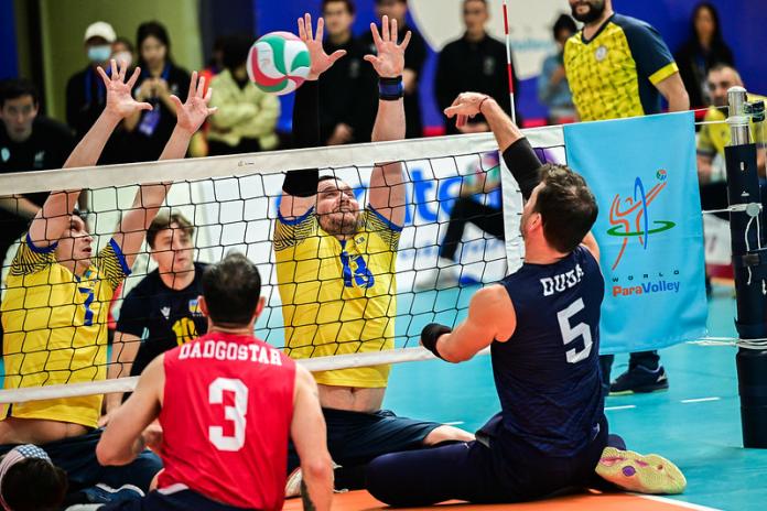 Two male athletes block the ball during competition. 