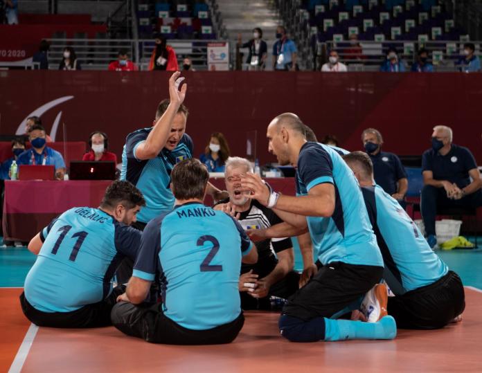 About five male sitting volleyball players form a circle on the court