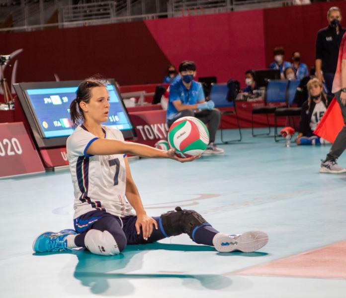 A female sitting volleyball athlete holds a ball before serving