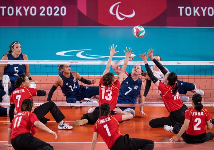 Two sitting volleyball athletes try to block the ball during a match.