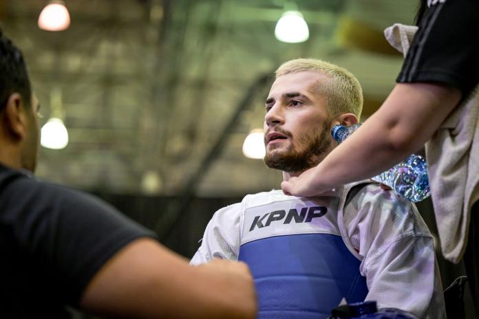 A close-up shot of a male Para taekwondo athlete. His coach is giving him a bottle of water