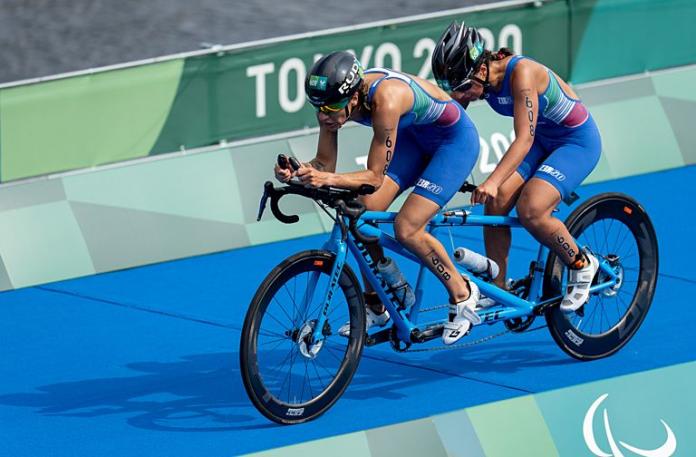 A female Para triathlete and her guide are competing on a tandem bike