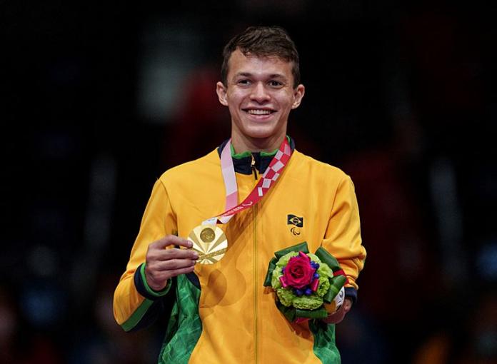 A male athlete wearing Brazil's yellow uniform poses for a photo after receiving a gold medal