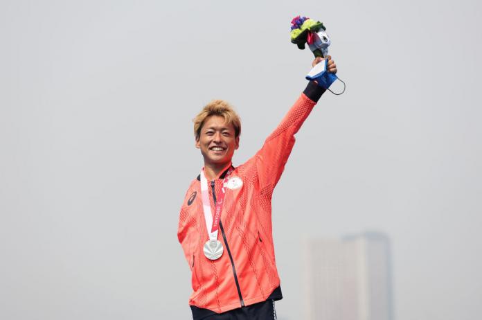 Male triathlete raises his left arm after receiving a silver medal