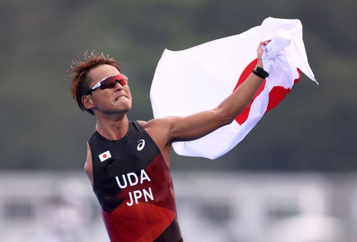 A male Para triathlete reacts after finishing a race. He is holding a flag of Japan