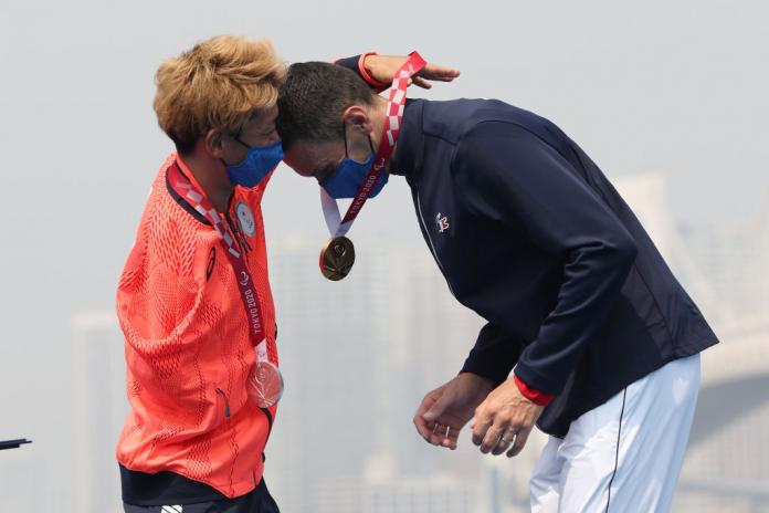 A male Para triathlete gives a gold medal to the athlete next to him