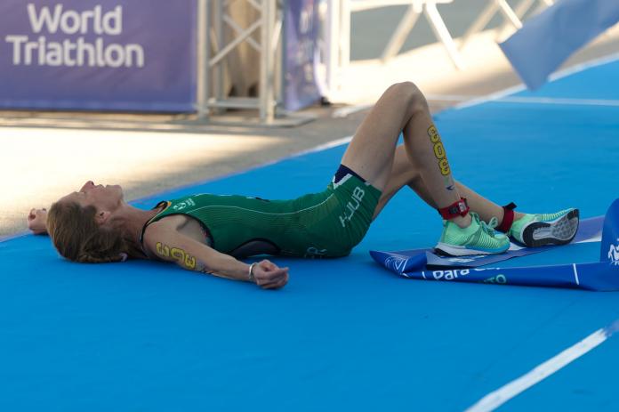 A female triathlete wearing South Afirca's green uniform is lying down after crossing the finishline