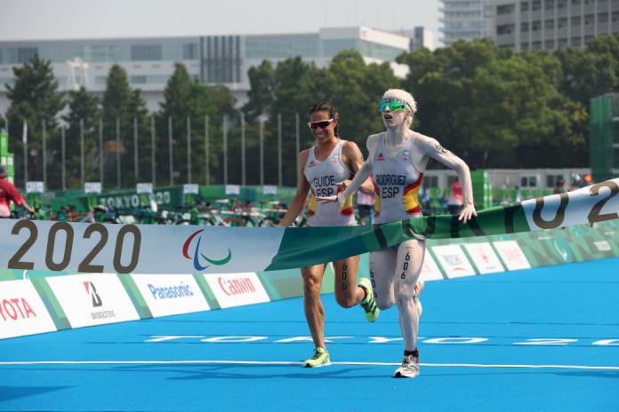 Two female athletes - one Para triathlete and her guide - crosses the finish line at the Tokyo 2020 Paralympics.