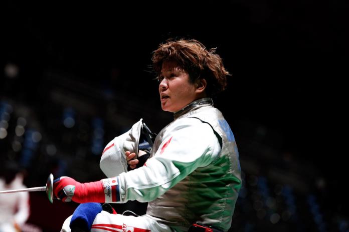A female wheelchair fencing athlete holds a mask and her weapon