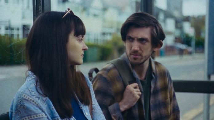 A close up image of a woman and a man speaking at a bus stop