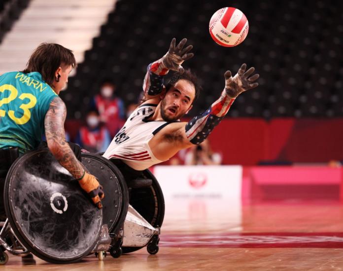 A male wheelchair rugby player throws a ball