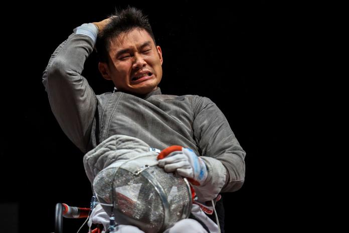 A male wheelchair fencing athlete reacts to his victory