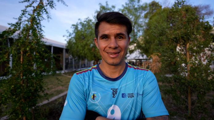 Jhon González, un futbolista ciego de Colombia, está parado afuera con un uniforme azul, cruzado de brazos