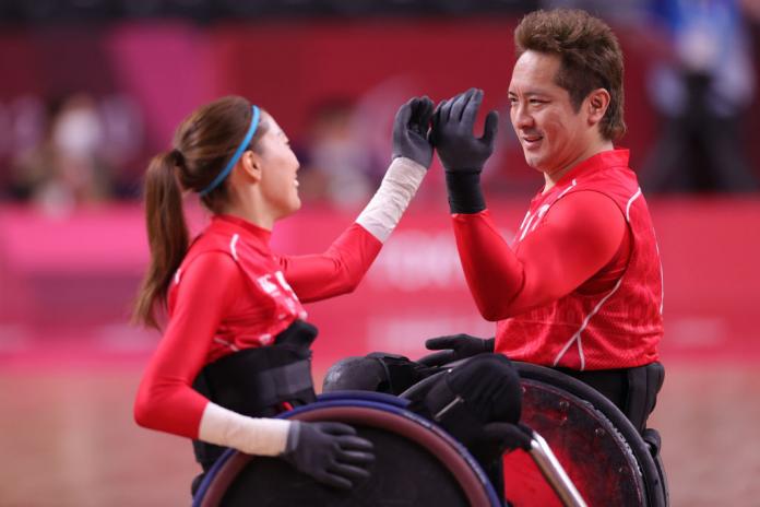 A male and female in red in wheelchairs raise their hands to high five