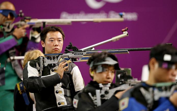 Shooting Para sport athletes are lined up for competition. One athlete is in focus, and holds his pistol.