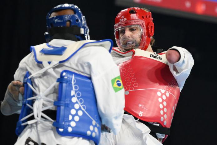 Two Para taekwondo athletes compete, with one in red facing the camera and kicking the other