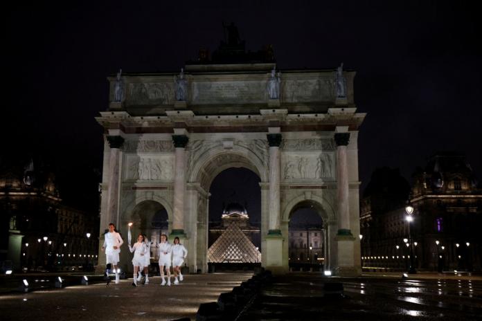 athletes running through the Arc de Triomph holding the Olympic torch 