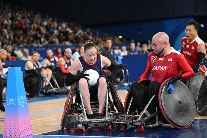 Sarah Adam of Team USA scorers a wheelchair rugby try in the corner of the court, with incoming pressure from an opposing Japanese player