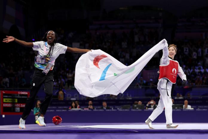 Zakia Khudadadi and her coach wave a flag with the Paralympic logo