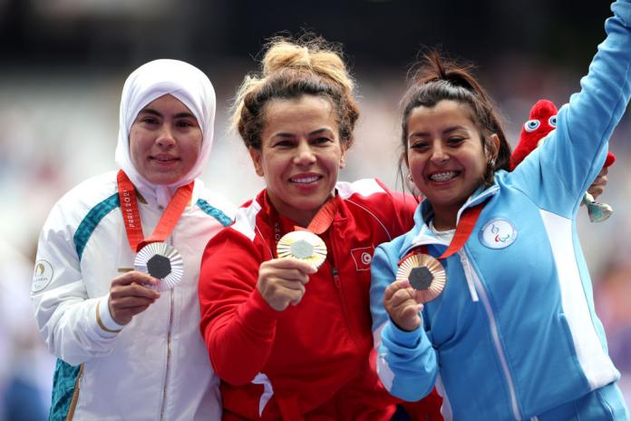 Three women's shot put medallists pose on the podium, holding their medals