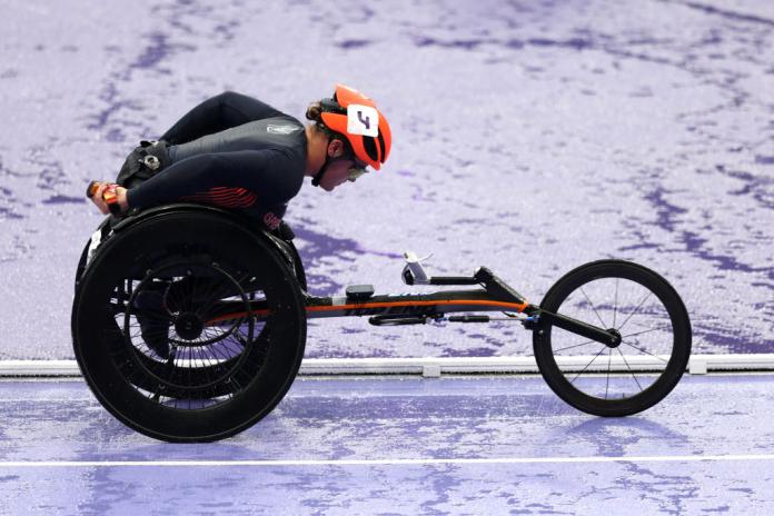 A woman in a racing wheelchair competes on a wet purple track