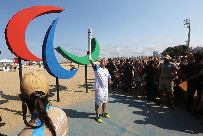 a man holding up the Paralympic torch in front of the Agitos symbol 