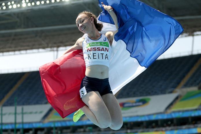 Para athlete Nantenin Keita jumps for joy high in the air holding the French flag inside the athletics stadium in Rio