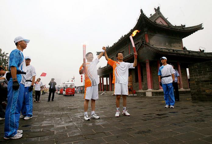 two men holding the Paralympic torch in front of a Chinese temple