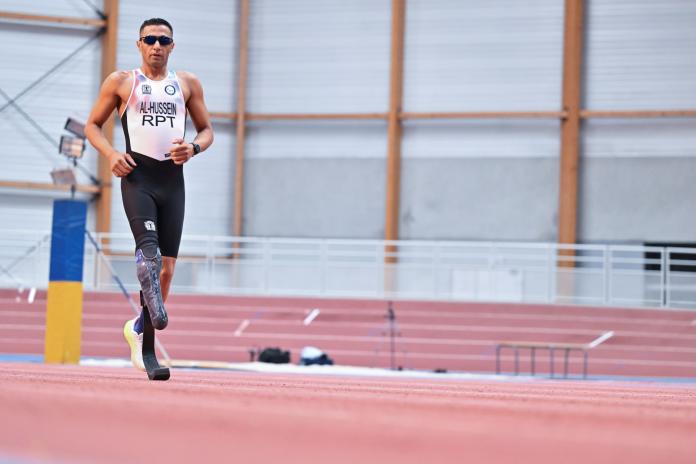 A male Para athlete runs on the track. He has a prosthetic running blade
