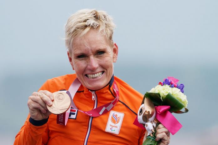 A female athlete wearing an orange uniform poses for a photo with a bronze medal.