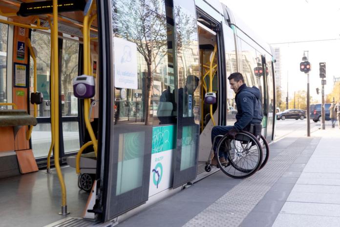 A man in a wheelchair getting on an overground tram. There are no steps between the tram and the platform