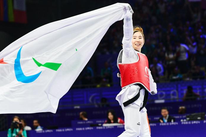 Zakia Khudadadi, a female Para taekwondo athlete, runs while holding the Paralympic flag with her right hand