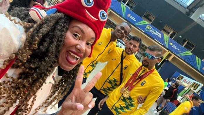woman in front in Phyrge hat makes peace sign with 3 Brazilian male athletes behind her