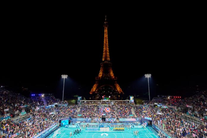 A wide image of the Eiffel Tower Stadium, Three teams are on the podium, in front of a packed crowd and the Eiffel Tower.