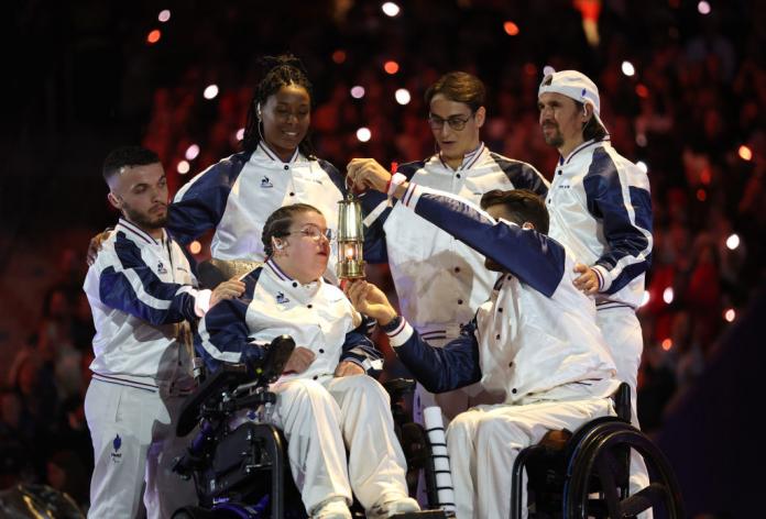 Aurelie Aubert apaga la llama paralímpica. Cinco atletas la rodean, uno de ellos sosteniendo una pequeña linterna frente a su cara