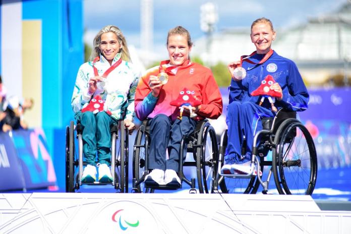 three female wheelchair racers on the podium holding up their medals