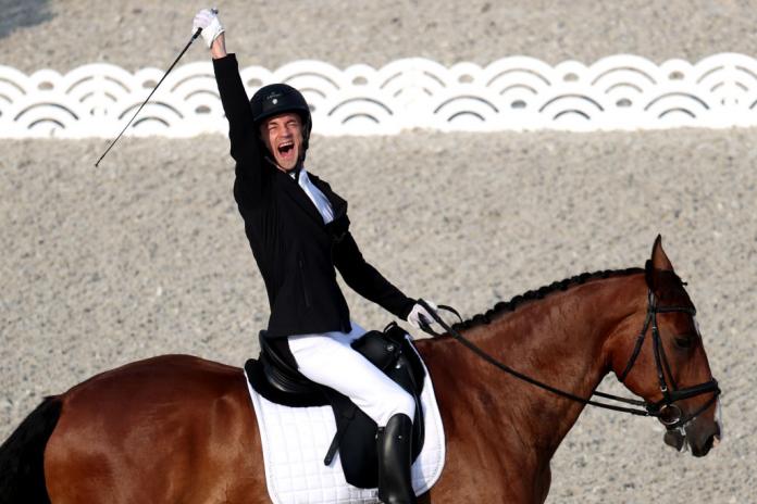 A man rides a horse and has one arm in the air, yelling in celebration