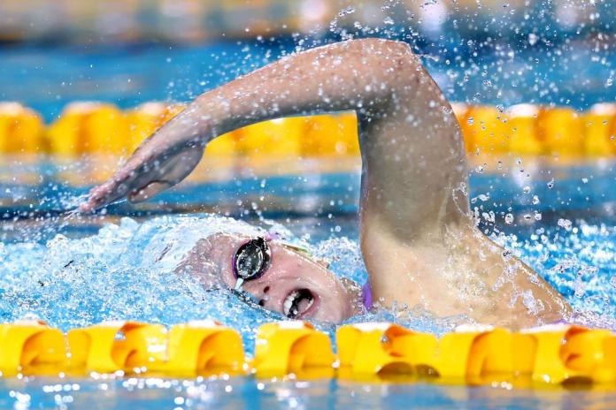 A swimmer wearing goggles races in the pool inside yellow lanes