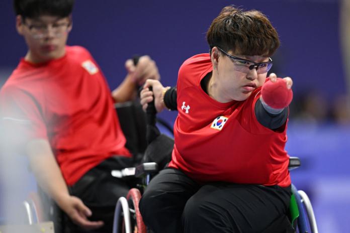 Vestido con una camisa roja, un jugador coreano de boccia apunta la bola roja a su objetivo