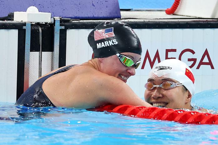 two female swimmers with caps on lean over the barrier and laugh together