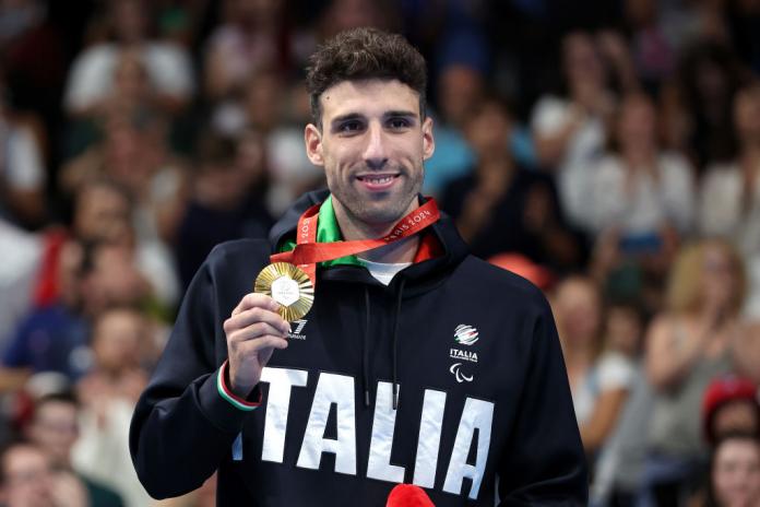 A man poses for a photo holding a gold medal
