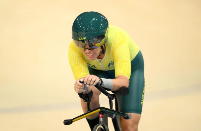 A Para cyclist in a bright yellow vest races at the indoor veladrone at the Paris 2024 Paralympics Games