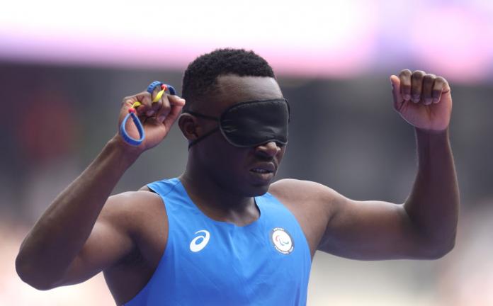 A man wearing an eye covering lifts his arms up in the air