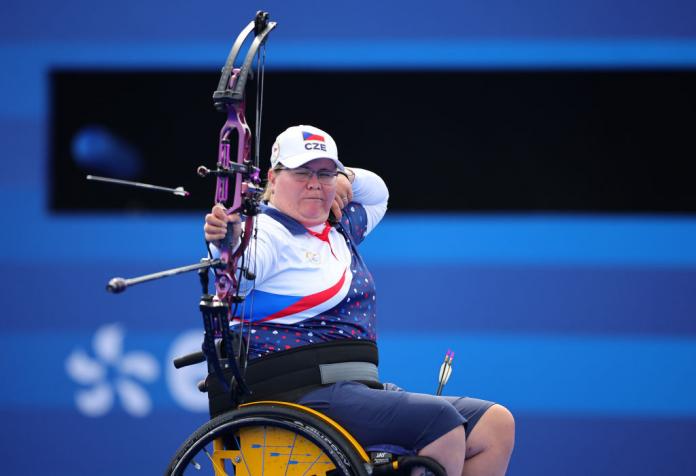 A woman in a wheelchair aims and releases an arrow from her bow