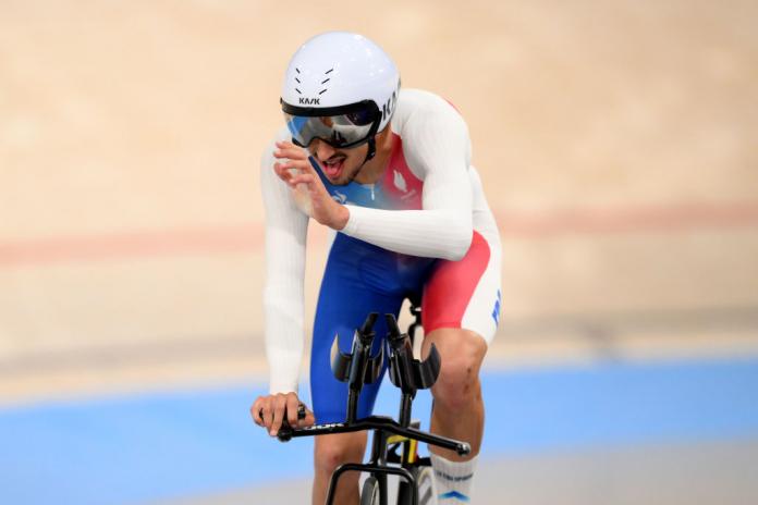 Un hombre monta una bicicleta en una pista de velódromo y levanta una mano en el aire para reconocer a la multitud