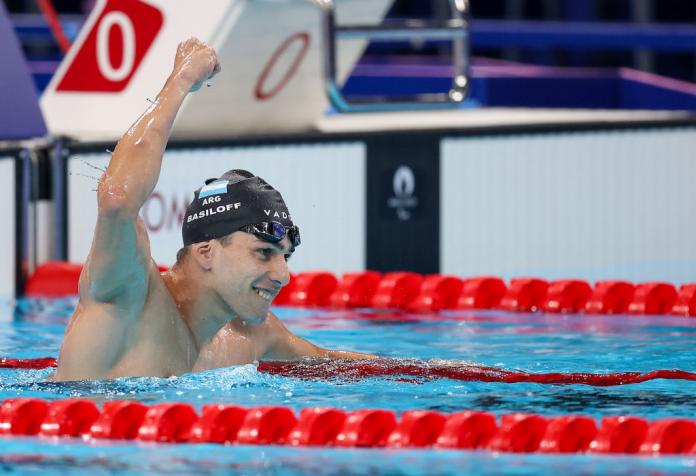 A man in a swimming pool raises one arm in celebration